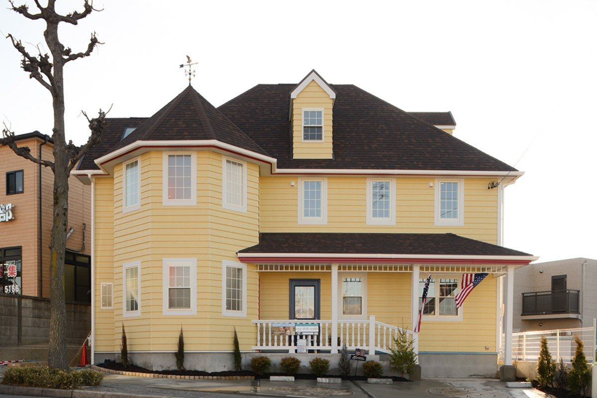アメリカンスタイルの黄色い外壁と三角屋根・白い窓枠とウッドデッキが